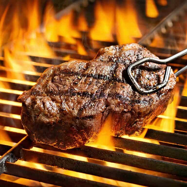Picture of a steak on the bbq with some tongs.