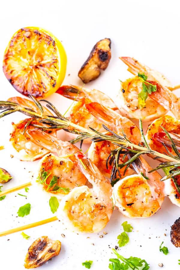 Grilled garlic shrimp on wood skewers on a plate with rosemary on top.