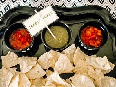 Overhead shot of chips and salsa with a sign for a zombie party.