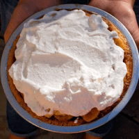 Overhead of a woman holding a pie topped with whipped cream.