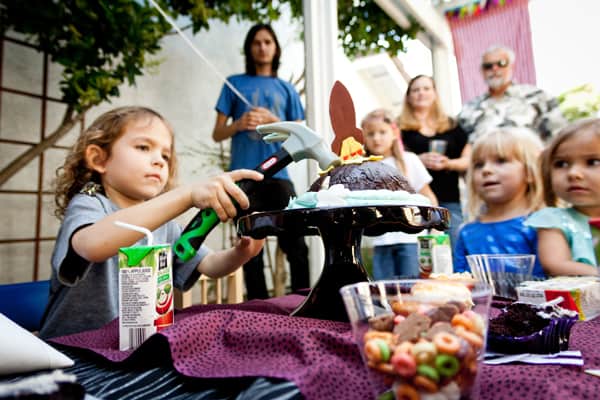 A kid using a hammer on a hard chocolate shelled cake. 