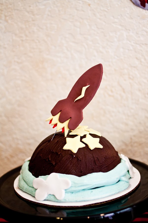 Close up of a chocolate rocket ship on top of a hard shell chocolate cake. 