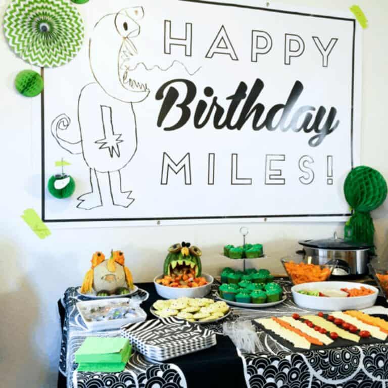A kid's party table with a wall sign with a big kid drawn monster drawn on it.