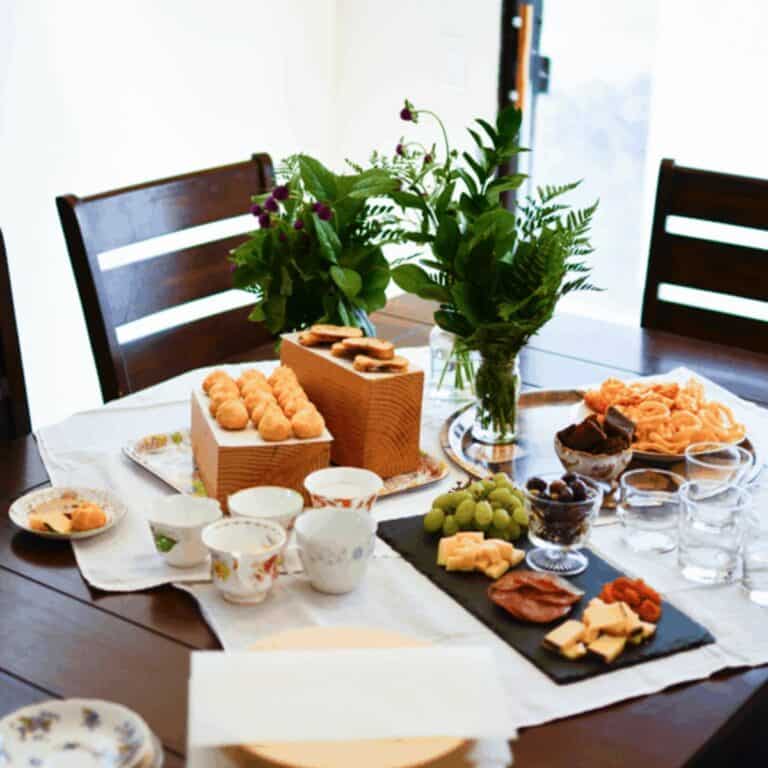 A party table with some small treats, flowers and tea cups.