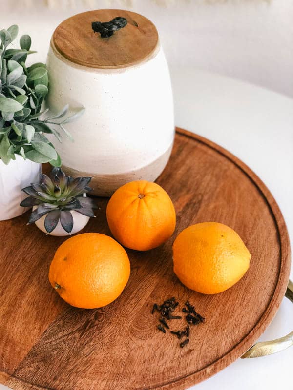 Decorative tray with oranges and whole cloves laying next to them.