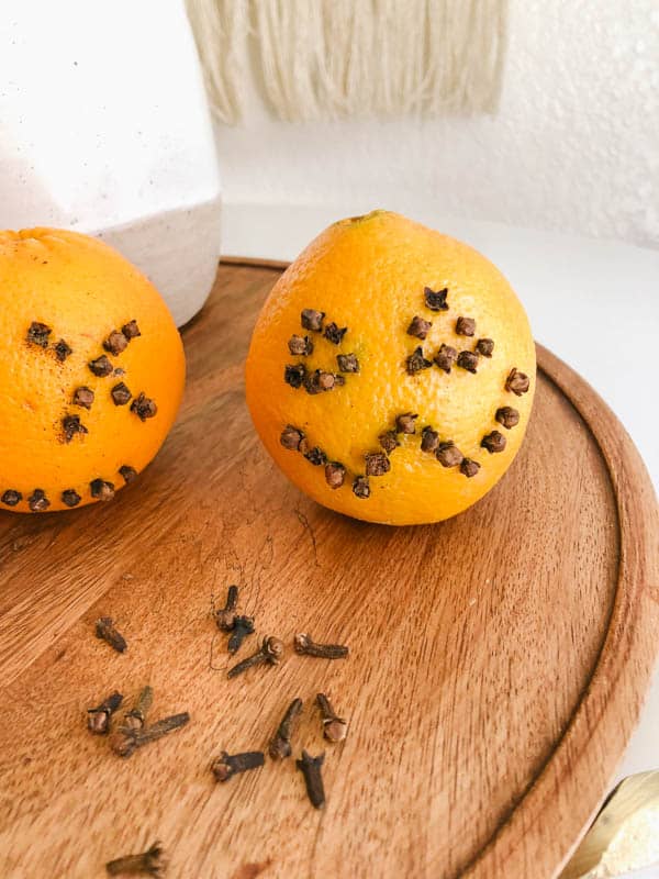 an orange on a tray with cloves stuck in to make it look like a pumpkin face.