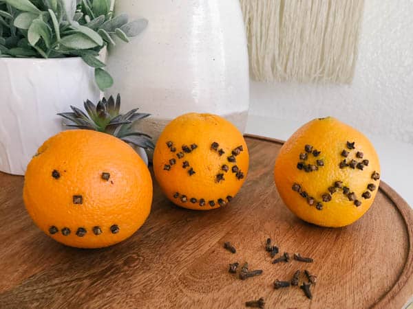 Oranges with pumpkin faces studded on them with whole cloves.