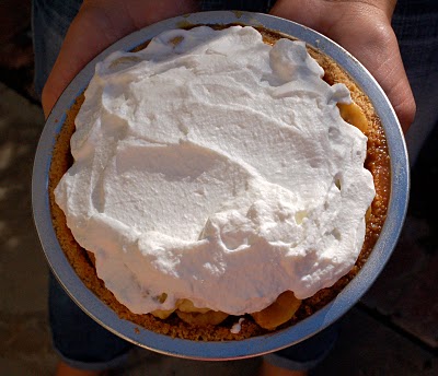Overhead shot of a mini banana pudding pie topped with whipped cream being held in a woman's hands. 