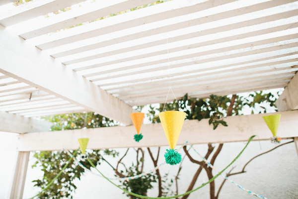 Party hats with yarn poms on the end hanging from a patio cover.