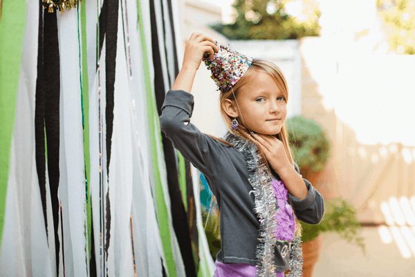 Little girl wearing a party hat in front of a photo booth wall. 