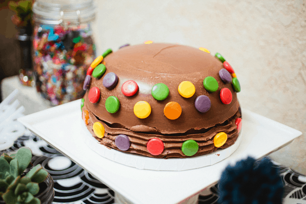 Chocolate birthday cake covered in candies on a cake plate.
