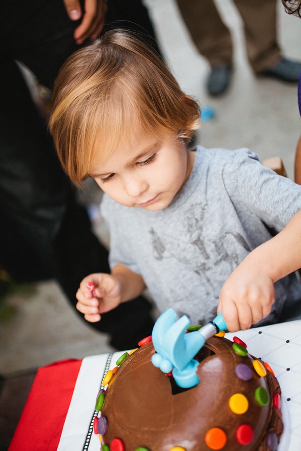 Kid using a toy hammer to break the hard chocolate shell of a birthday cake. 