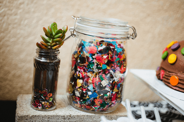 A glass jar full of confetti next to a small succulent.