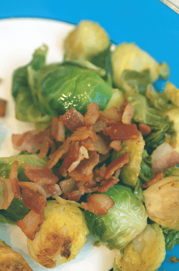 Blue rimmed plate with braised Brussels sprouts topped with crispy bacon pieces. 