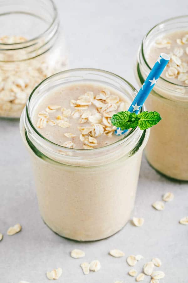 Banana oats smoothie or milkshake in glass mason jars on a gray stone background.