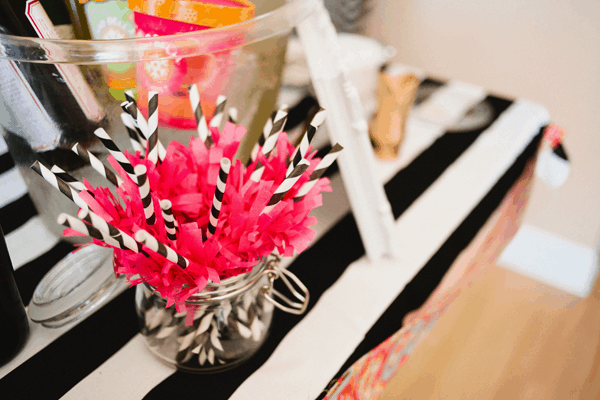 Close up of black and white striped straws with pink fringe decorations on them. 