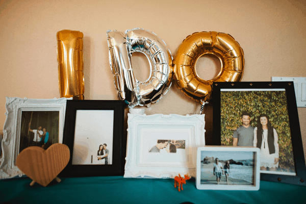 A table full of photos and small mylar balloons that say "I do."