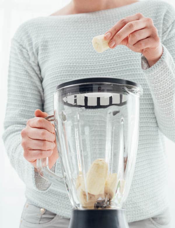 Woman putting a banana in a blender and preparing a delicious healthy smoothie in her kitchen.