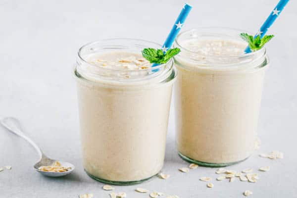 Banana oats smoothie or milkshake in glass mason jars on a gray stone background.