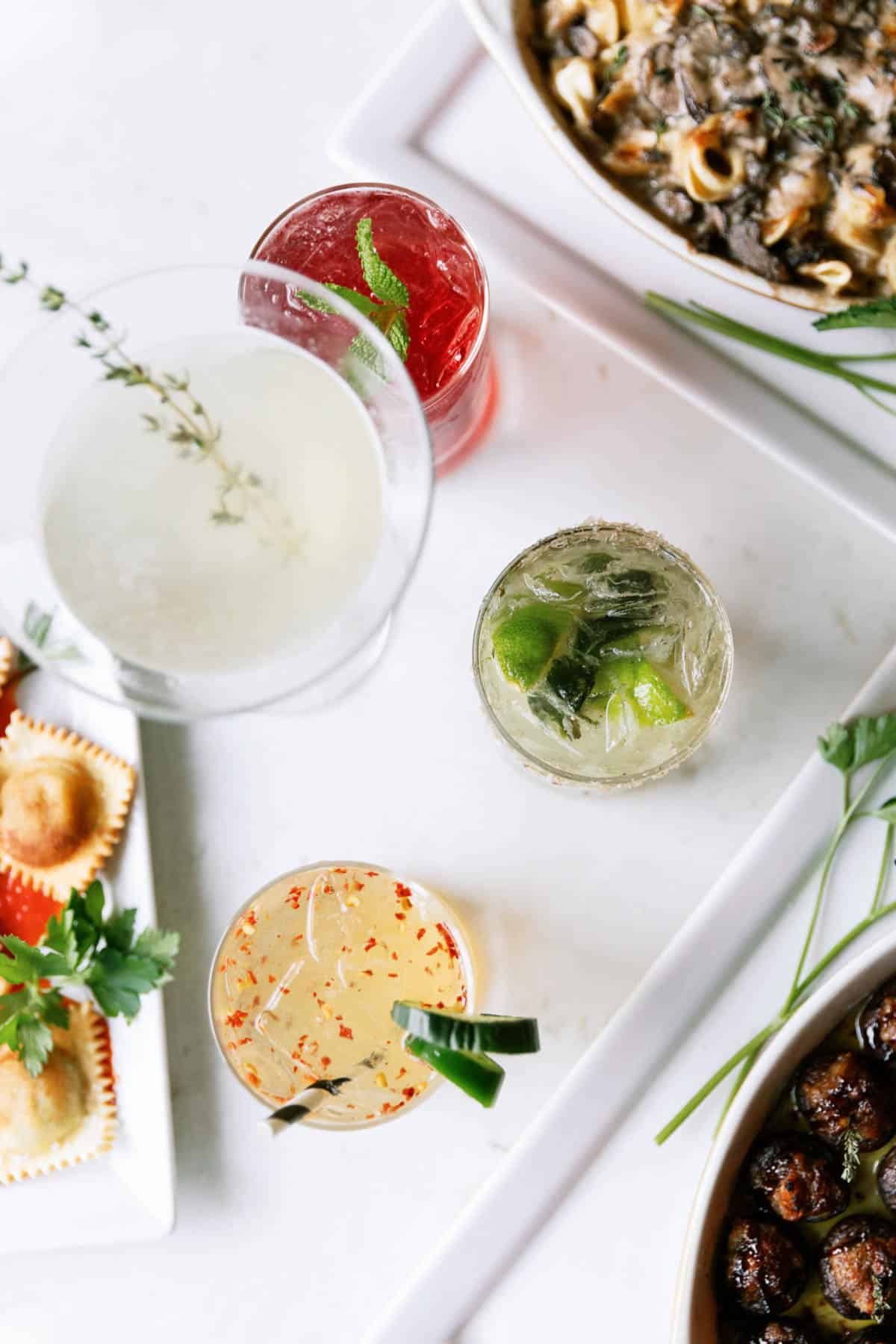 A white tray with several cocktails on it next to food for a party.