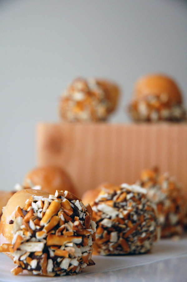 Pretzel pieces stuck to chocolate on the bottom of donut holes on a white table with wooden block stand in the back. 