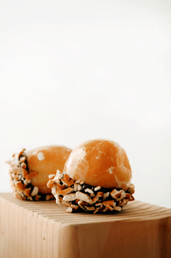 Donut Holes dipped in chocolate and crushed pretzel pieces on a wooden block.