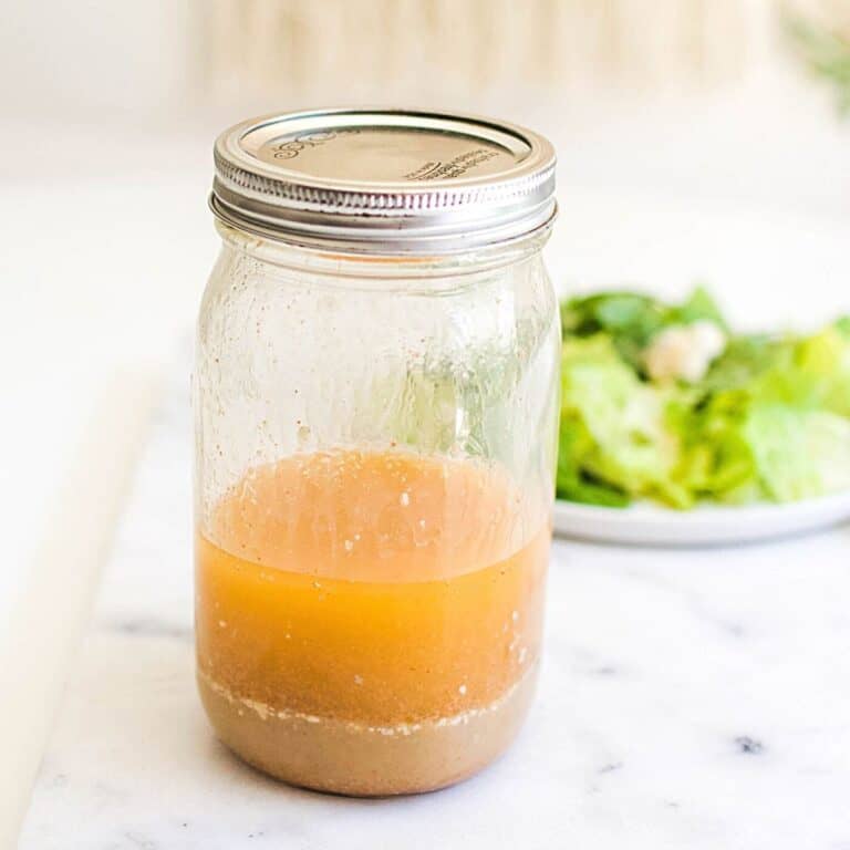 A jar holding homemade blue cheese vinaigrette salad dressing on a table next to a plate of salad.