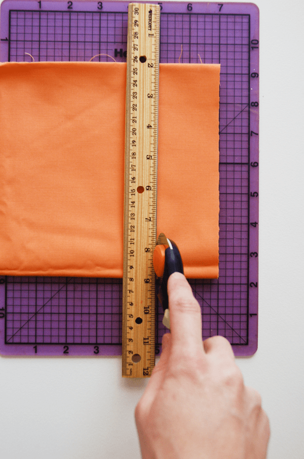 A woman using a rotary cutter to cut some fabric into a strip. 