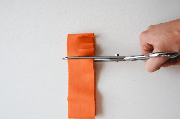 A woman making a cut with scissors on a folded over strip of fabric. 