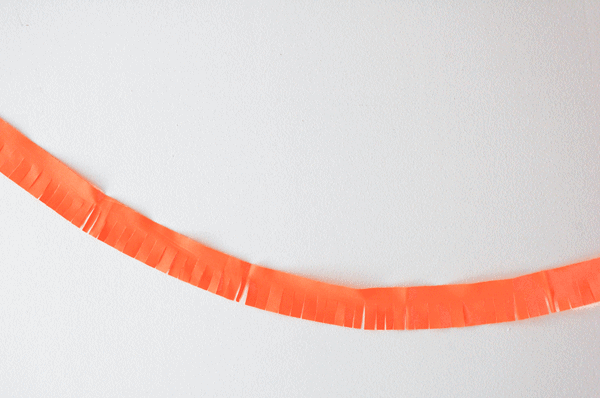 A strip of orange fabric taped like a garland on a wall that has been fringed.