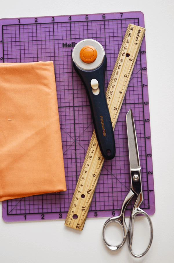 A rotary blade, ruler, scissors and fabric sitting on a craft board. 