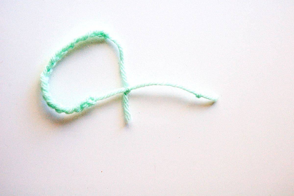 A mint green adjustable yarn bracelet on a table.