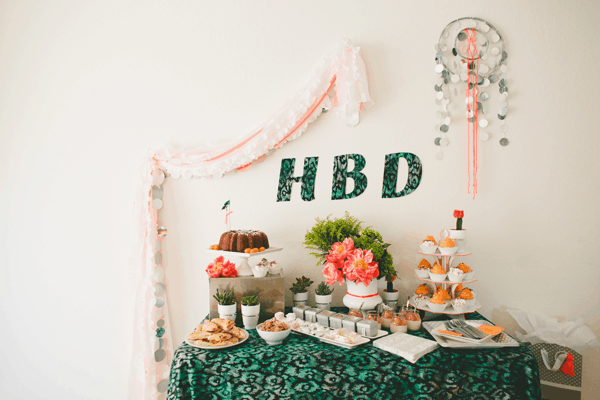 A dessert table for a party with a sign on the wall that says "HBD" which stands for happy birthday. 