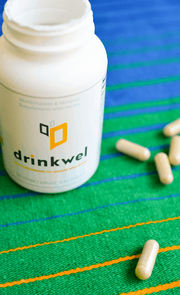 Bottle of Drinkwel hangover helper on a table next to some capsules. 