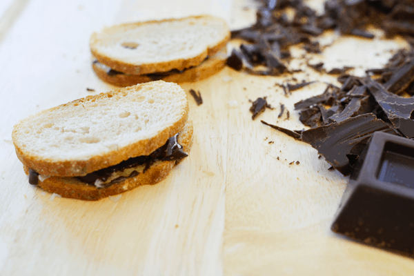 Chocolate and sea salt sandwiches next to chopped dark chocolate on a cutting board.