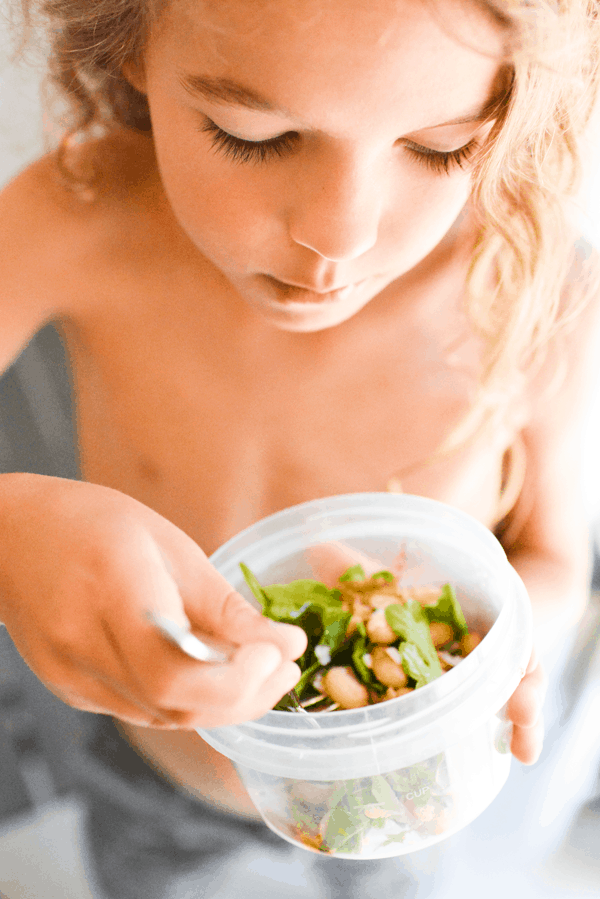 Kid eating salad with white beans and arugula out of abowl. 