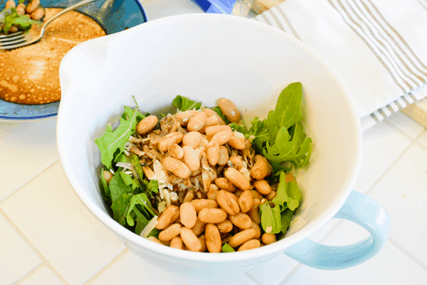 A large bowl of salad with arugula and cannellini beans. 