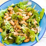 A blue bowl of salad with arugula, white beans and parmesan on a table.