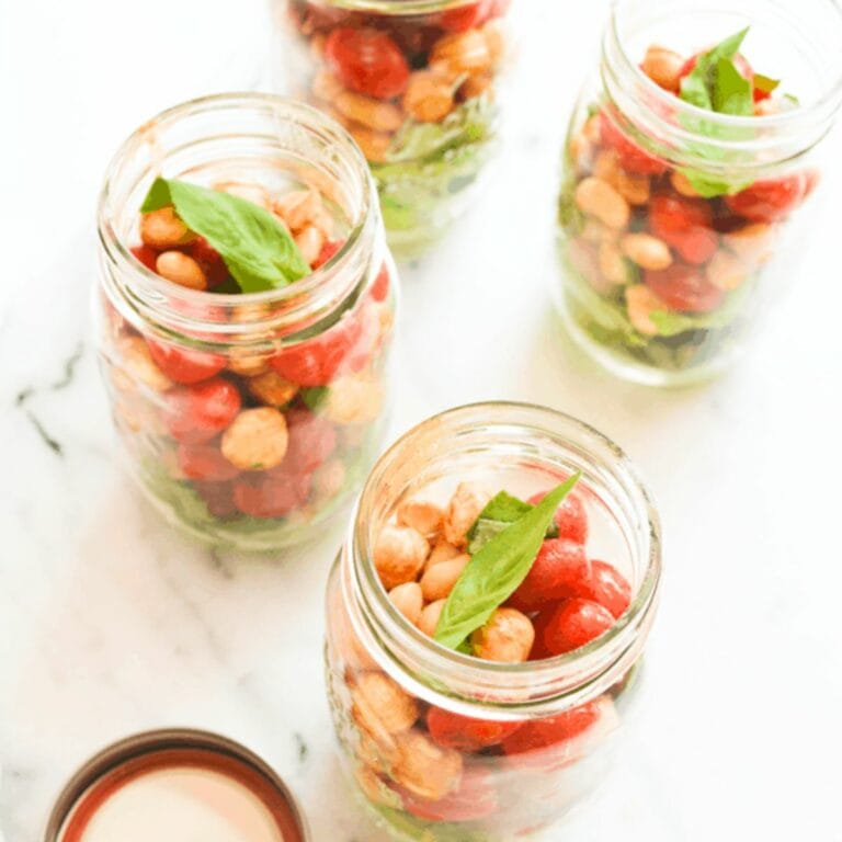 Glass jars on a table holding a Caprese Salad made with white beans.