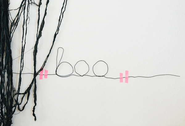 wire twisted to say the word "boo" taped to a wall with pink tape next to spooky black Halloween fabric