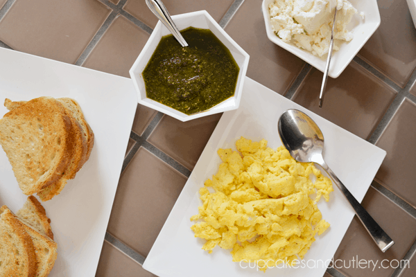 Overhead shot of plates of toast, scrambled eggs, and bowls of pesto and goat cheese. 