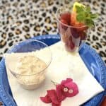 Close up of a cup holding a portion of churro fruit dip on a plate next to a cup holding fresh fruit.