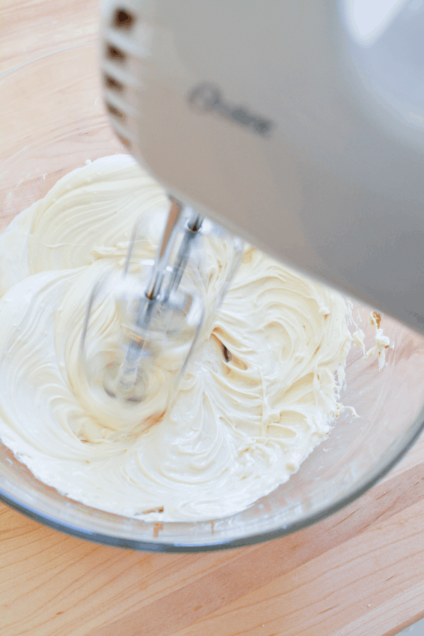 A bowl with cream cheese dip being mixed by a hand mixer. 