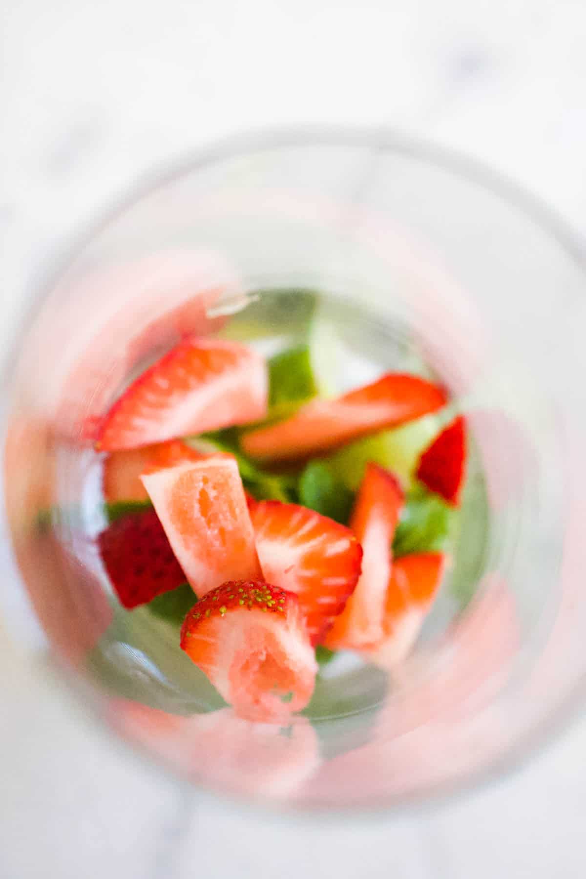 Pieces of strawberry, mint leaves and raw ginger slices in the bottom of a glass.