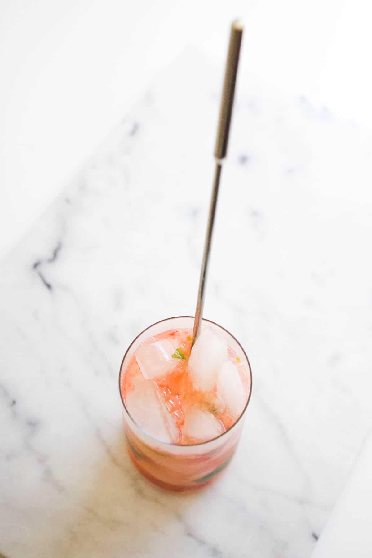 A top down view of a glass with ice and strawberry sparkling water with a long handled spoon.