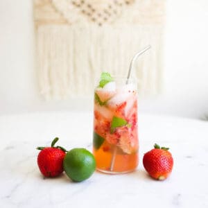 A glass with muddle fruit in sparkling water with a straw on a table.
