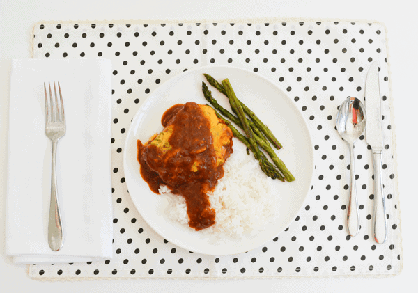 Tomato sauce and cheese topped pork chops on a dinner plate with asparagus next to it. 