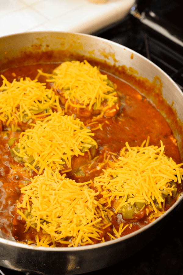 Pork chops topped with cheddar cheese in a pan on the stove. 