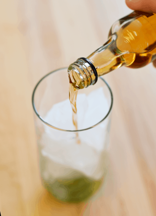 Pouring rum in a glass with ice on top of fresh lime and mint. 