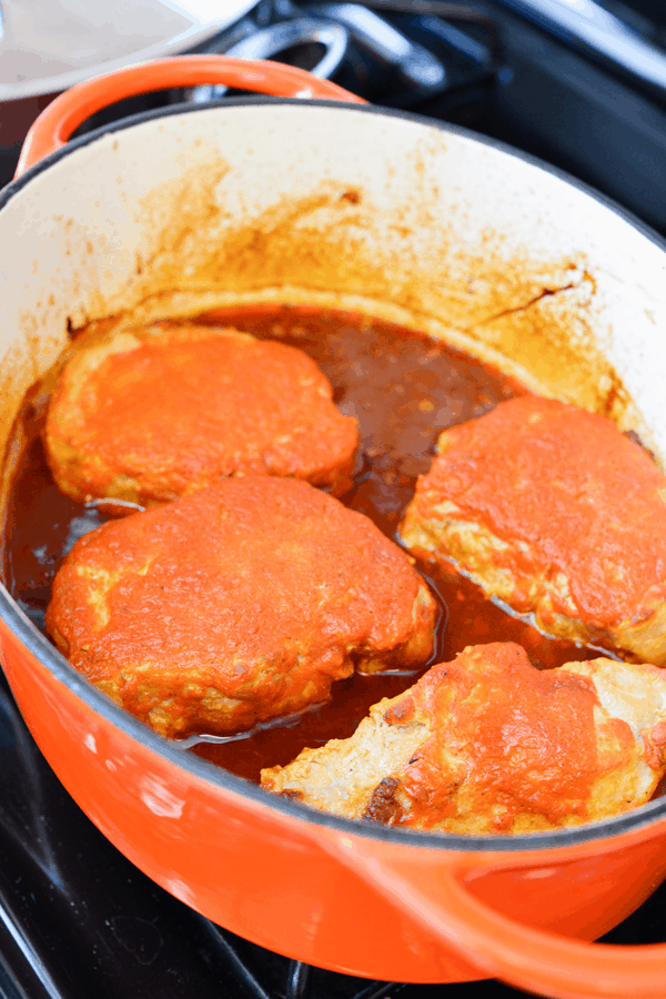 Close up of pork chops in a pan covered in sauce.